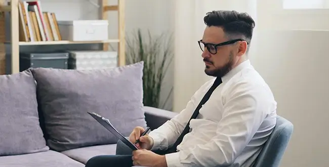 A male therapist writing on a clipboard during a session. 