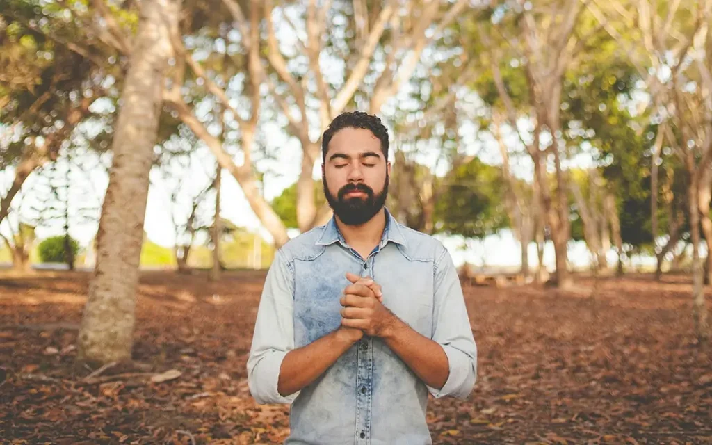 A man holding his hands over his chest while his eyes are closed